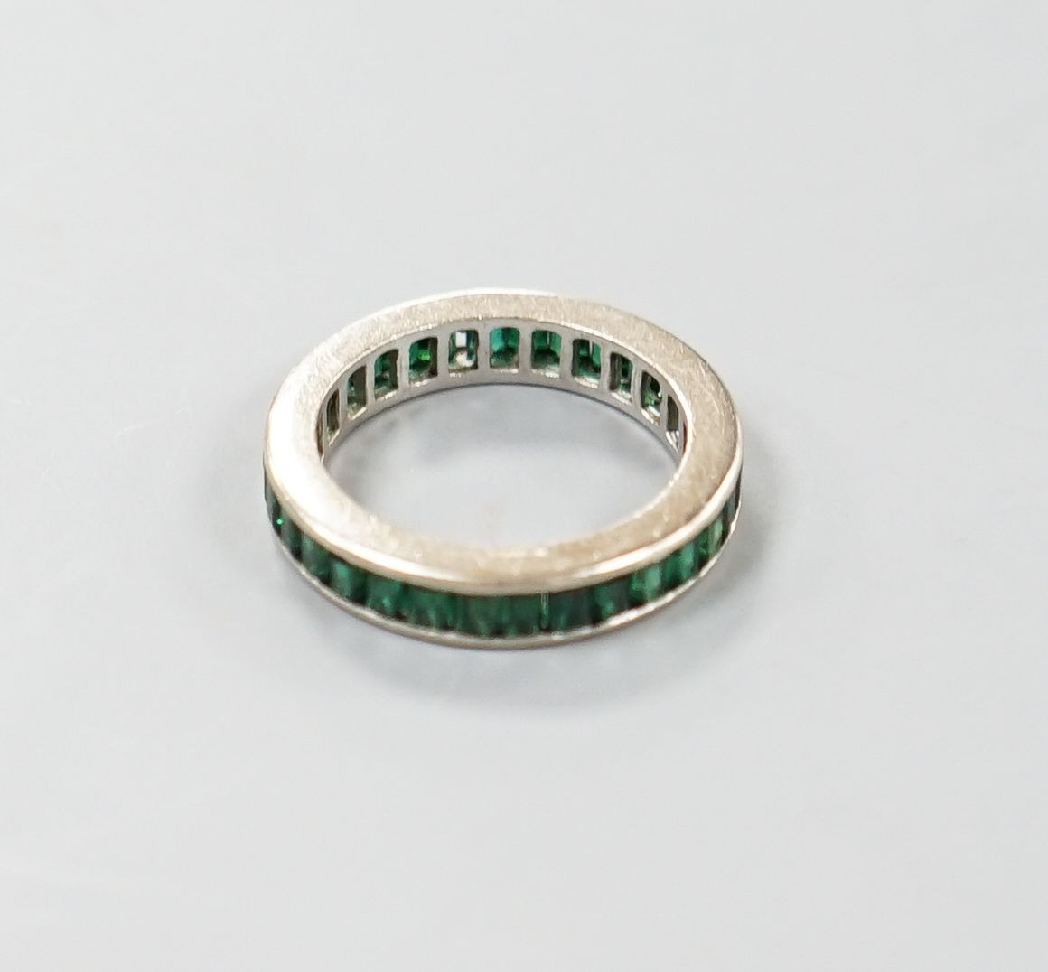 A white metal and green garnet? set full eternity ring, size L, gross weight 3.3 grams.